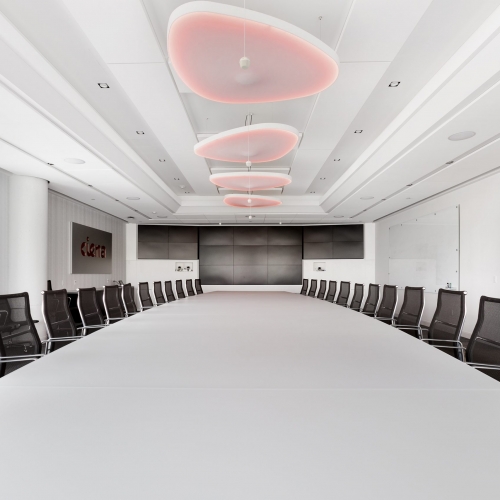 A row of Luceplan acoustic Petale light fixtures hung over a boardroom table, using colour tuning RGB technology these lights are set to red to match Ciena's branding