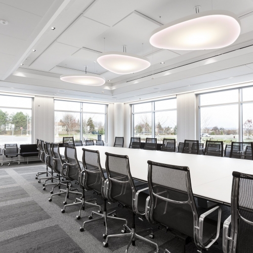 A row of Luceplan acoustic Petale light fixtures hung over a boardroom table, using colour tuning RGB technology these lights are set to red to match Ciena's branding