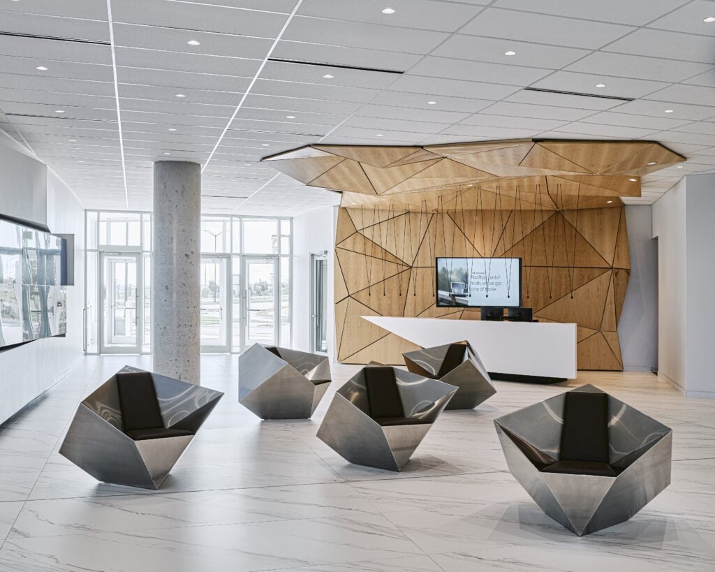 Reception at Kinaxis headquarters, Kanata — faceted timber origami ceiling with recessed downlights and Vibia Match pendants over the angular white desk