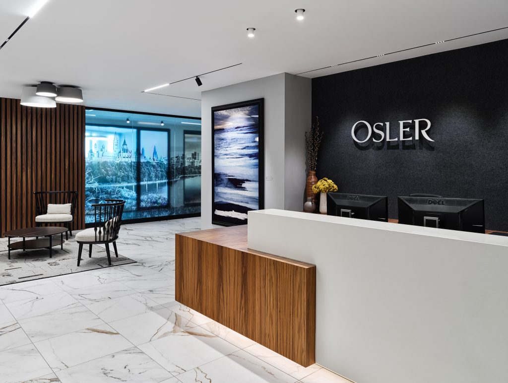 Reception at Osler’s Ottawa office, where track lighting grazes framed artwork on the OSLER feature wall and concealed LED tape edge-lights the wood desk.