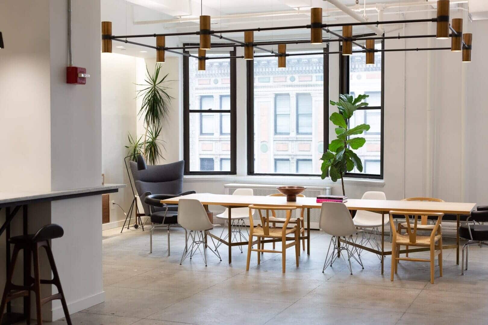 A loft office dining area with black branch pendants and tall windows admitting daylight
