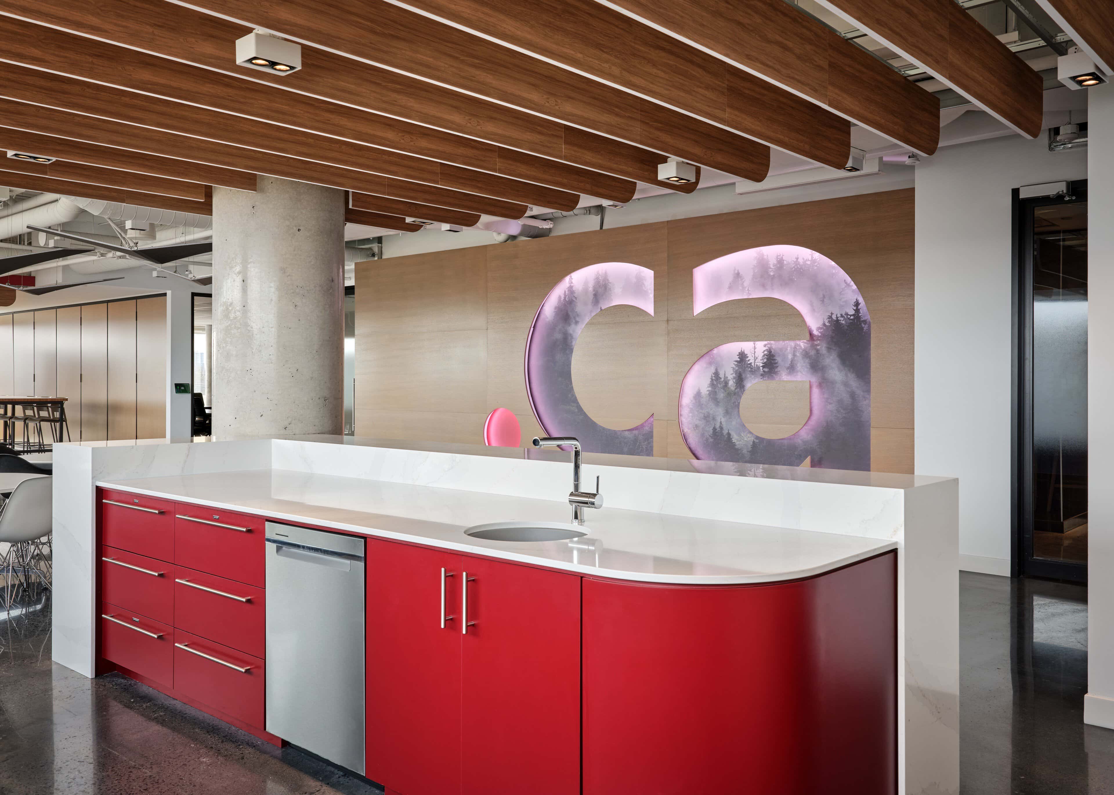 Backlit .ca letters with forest imagery above the CIRA kitchen island, under a wood-slat ceiling with integrated linear light