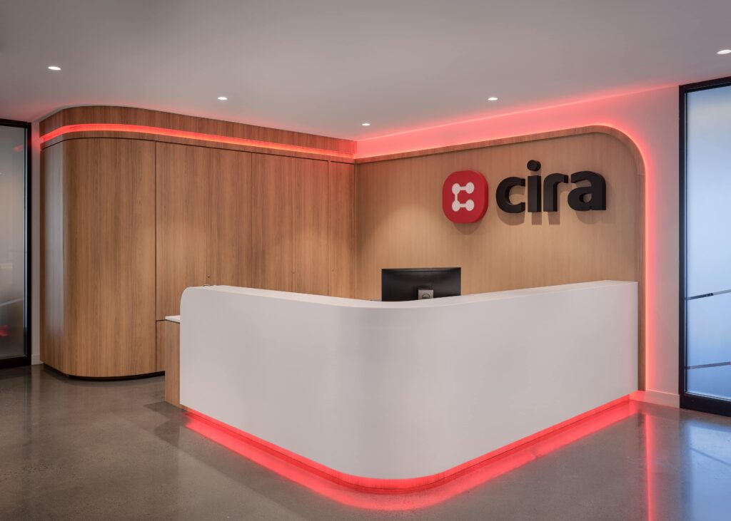 Nova Flex RGBW cove lighting in red, wrapping the curved walnut millwork header and the underside of the reception desk at CIRA, Ottawa