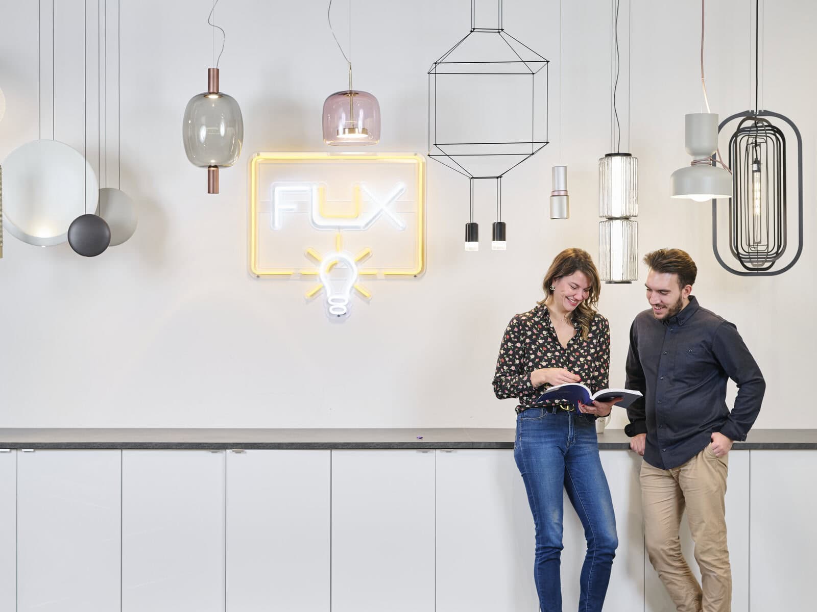 Two people reviewing lighting selections at a showroom pendant-light wall with a Flux sign.