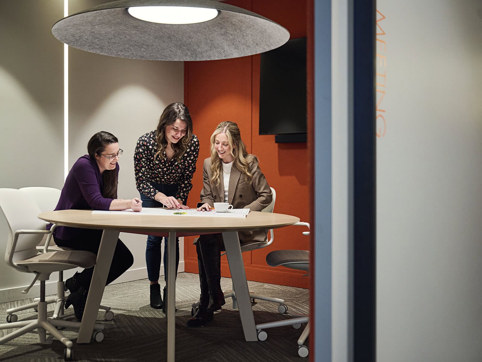 Four team members in a project meeting at a table under a disc ceiling light.