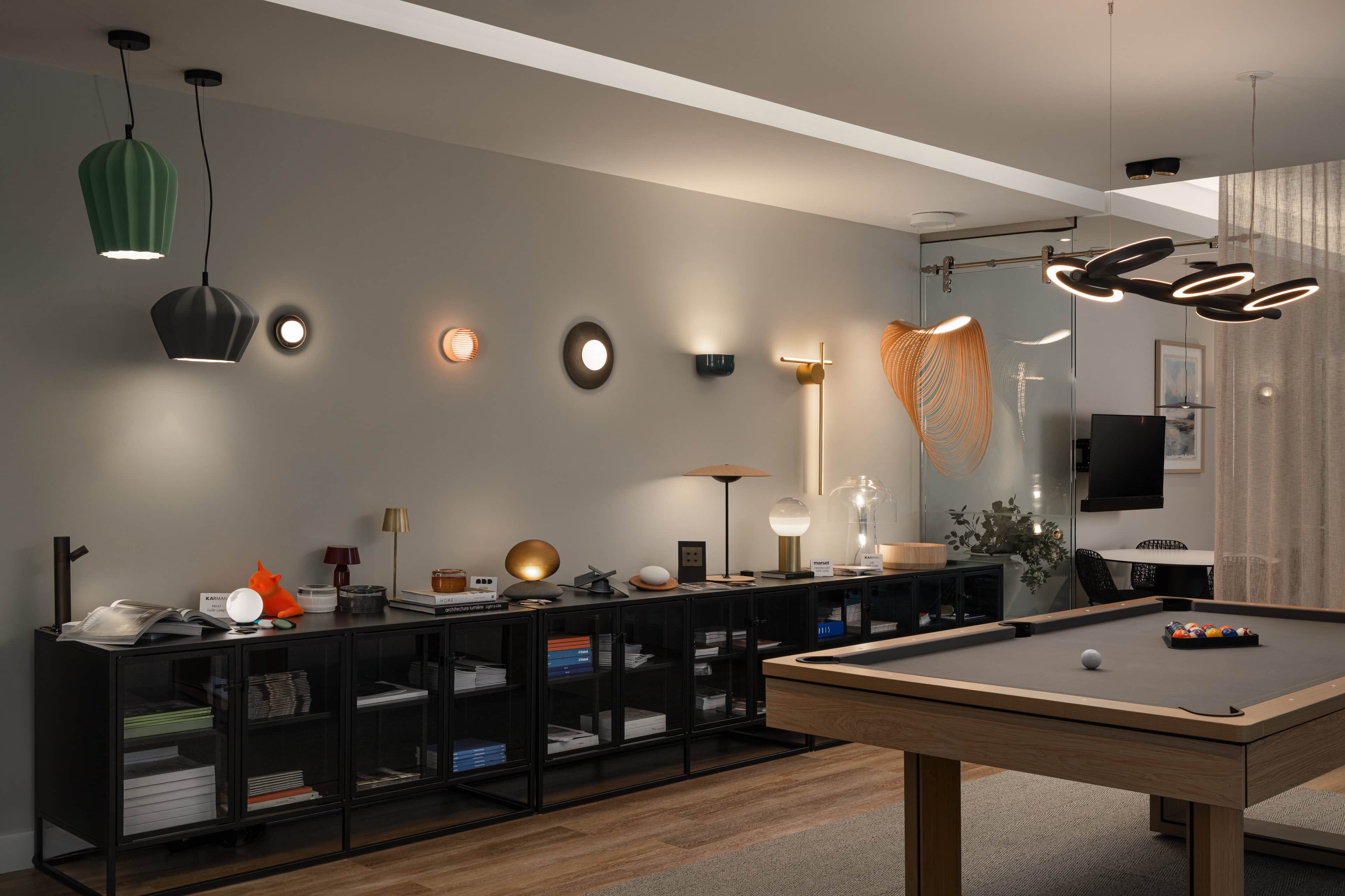 Flux Lighting showroom, Ottawa — a console wall of lit table lamps, pendants and sconces beside the games table.