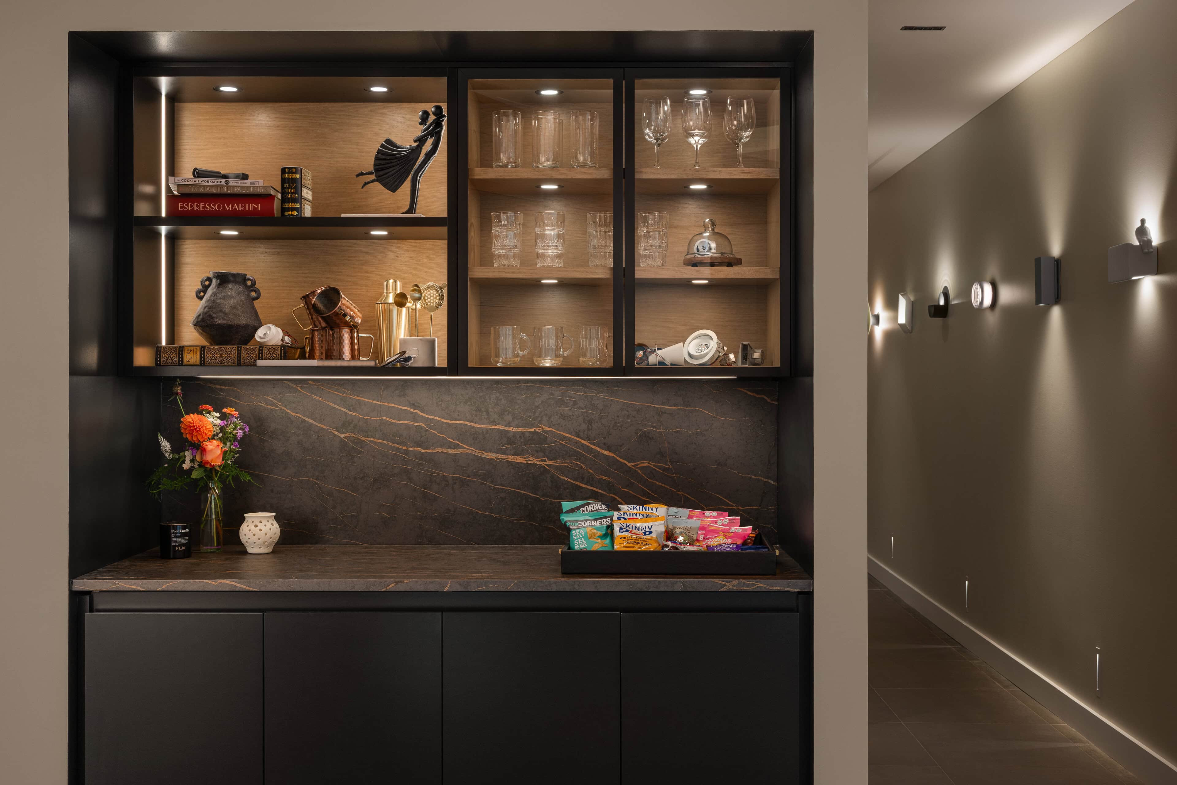 Flux Lighting showroom, Ottawa — a lit display cabinet of glassware and objects, beside a corridor washed by wall sconces.