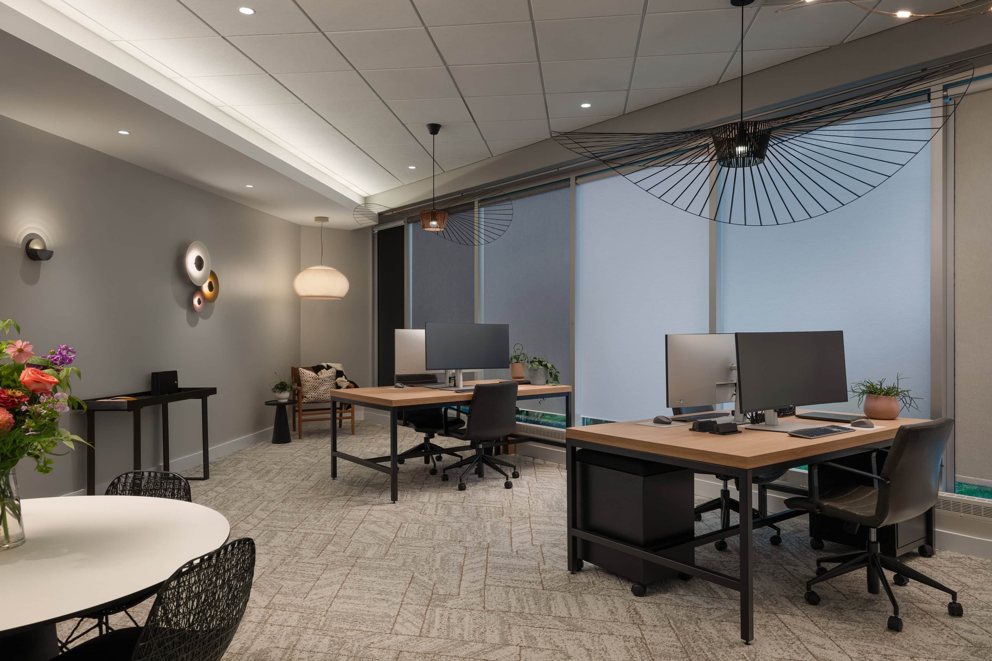 Flux Lighting showroom, Ottawa — the open office area, with desks under a wide wire pendant, a lit cove overhead and roller shades on the glazing.