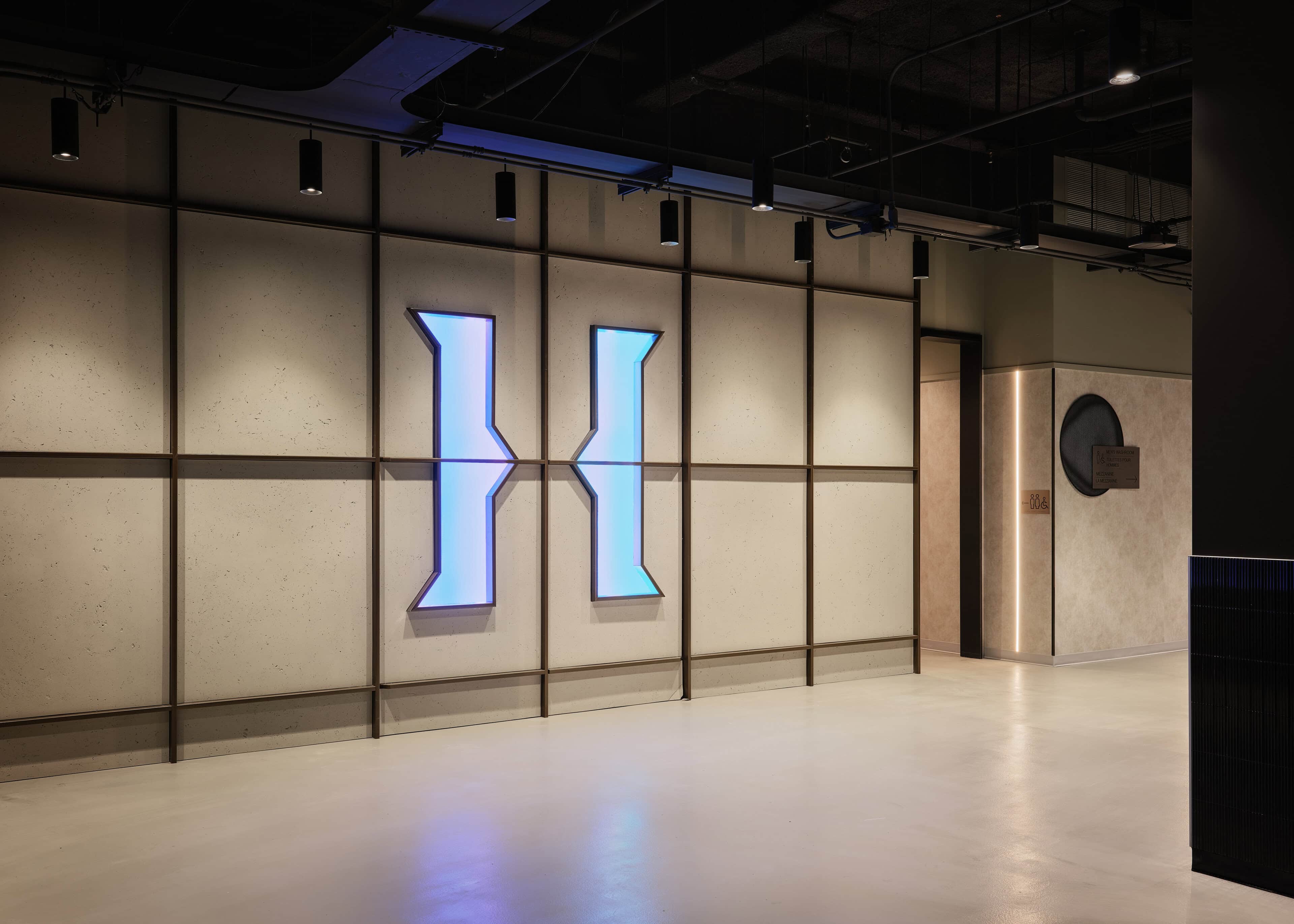 The entry vestibule at HISTORY Ottawa, a large backlit iridescent H set into a gridded wall above a polished floor
