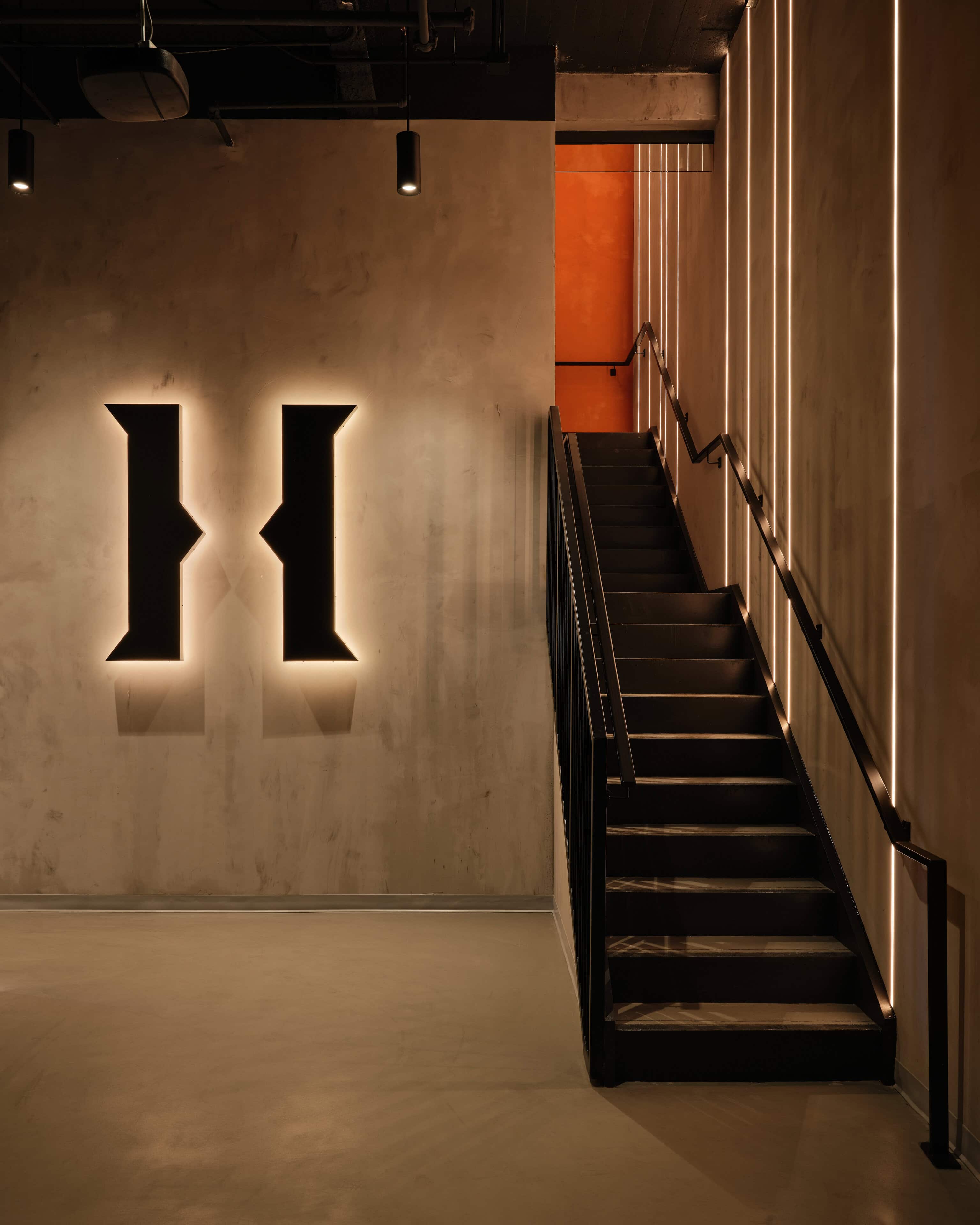 The entry stair at HISTORY Ottawa, with a backlit H cut into the wall and lines of light running up beside the flight
