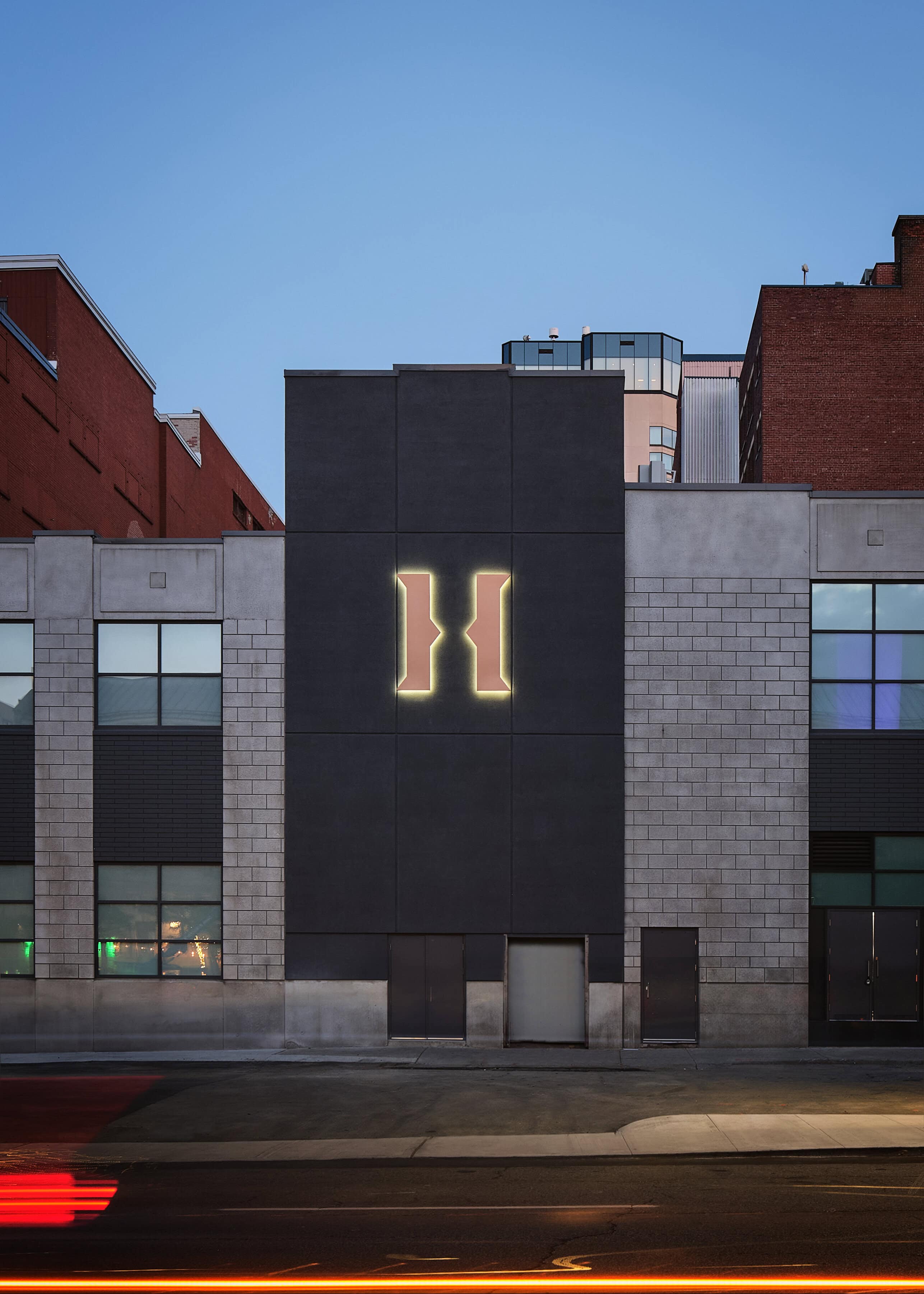 The George Street elevation of HISTORY Ottawa at dusk, a large illuminated H on the dark upper wall above the pale base