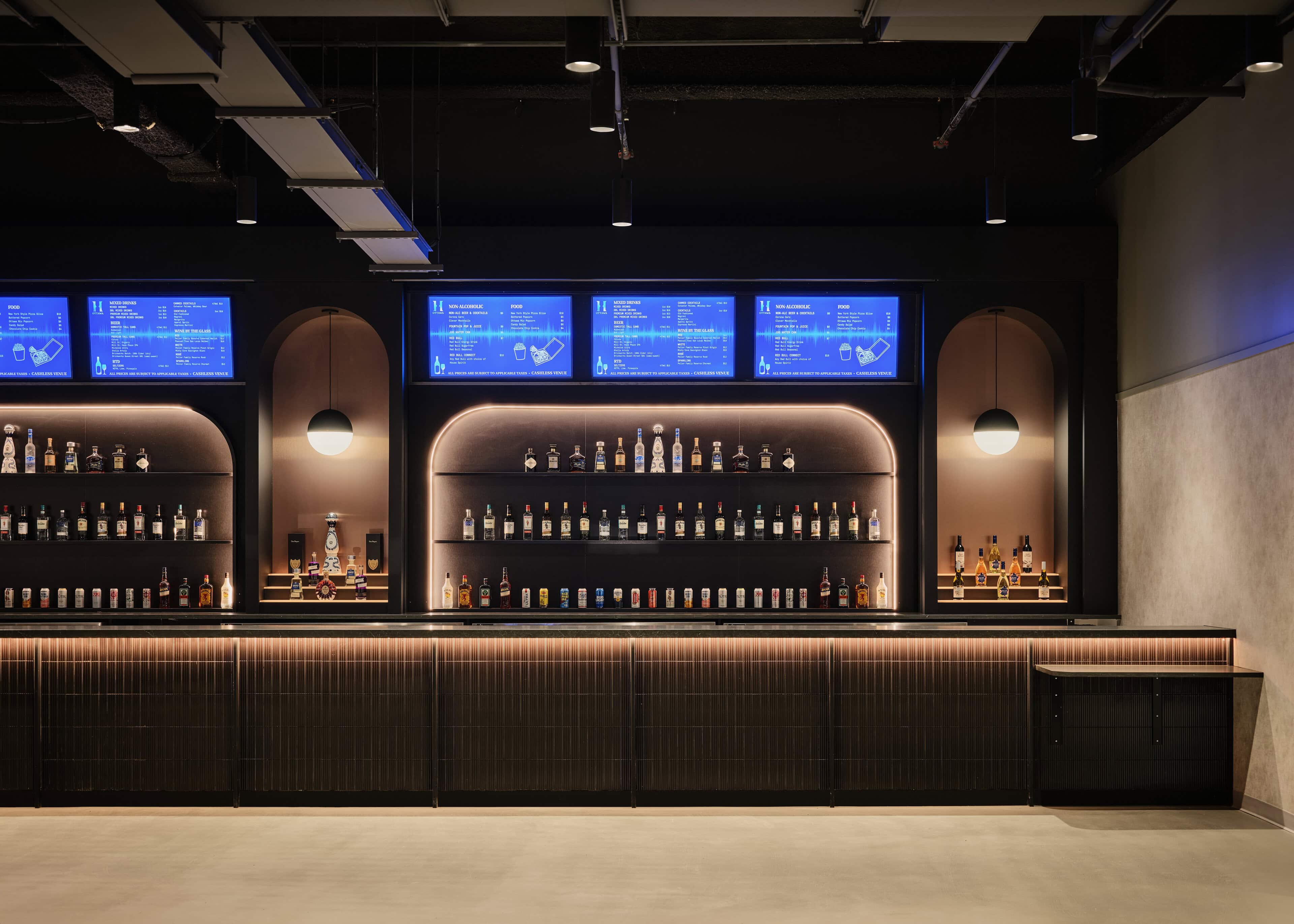 A Visual Comfort Akova globe pendant hanging in an arched backbar niche at HISTORY Ottawa, with lit bottle shelving below