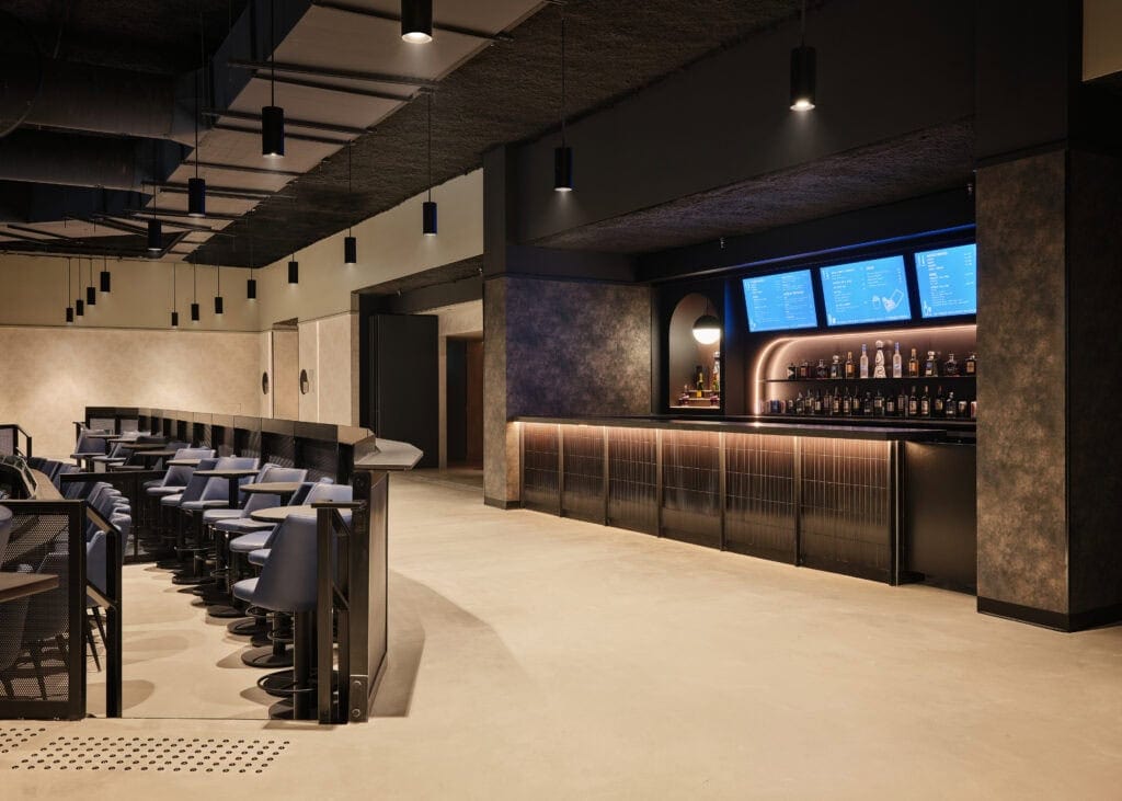 The mezzanine bar at HISTORY Ottawa, a row of black pendant cylinders over the counter and an illuminated backbar with screens above